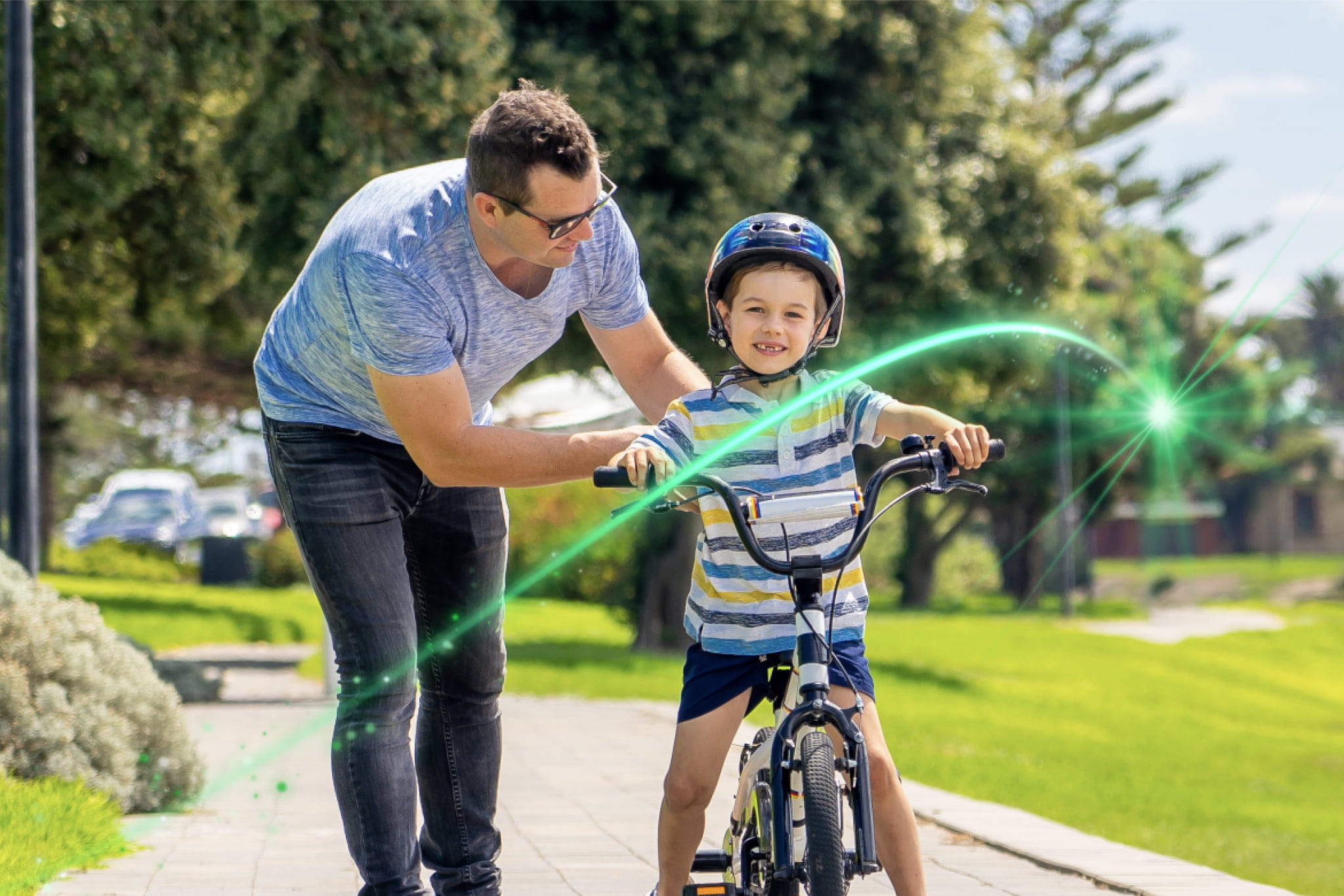 A young boy riding a bicycle in a local park with his dad supporting him