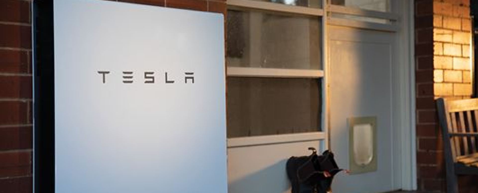 A Tesla solar battery installed on an exterior red brick wall outside a home