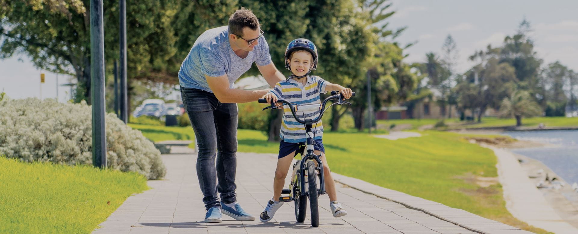 A father helping his son learn to ride a bike in a park