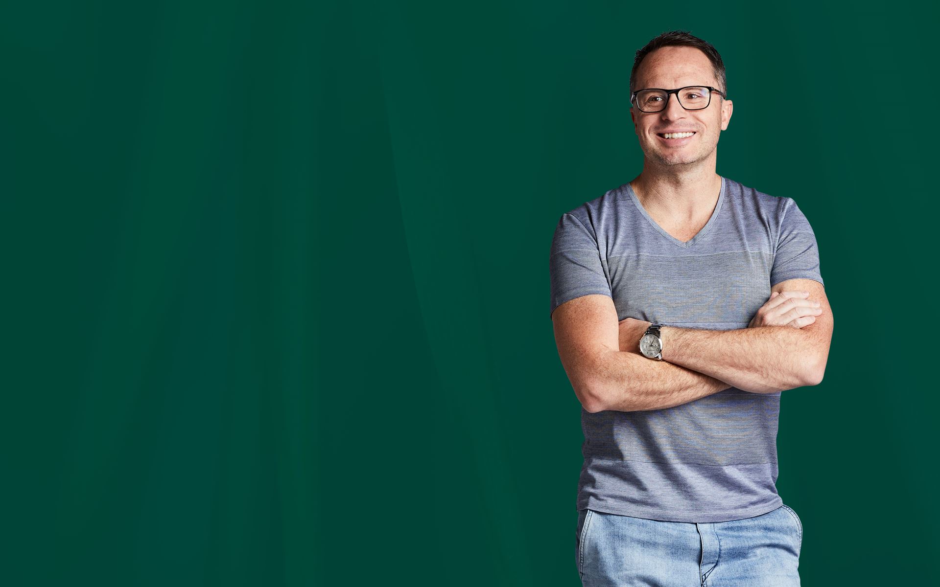 Man standing with his arms crossed in front of a green background.