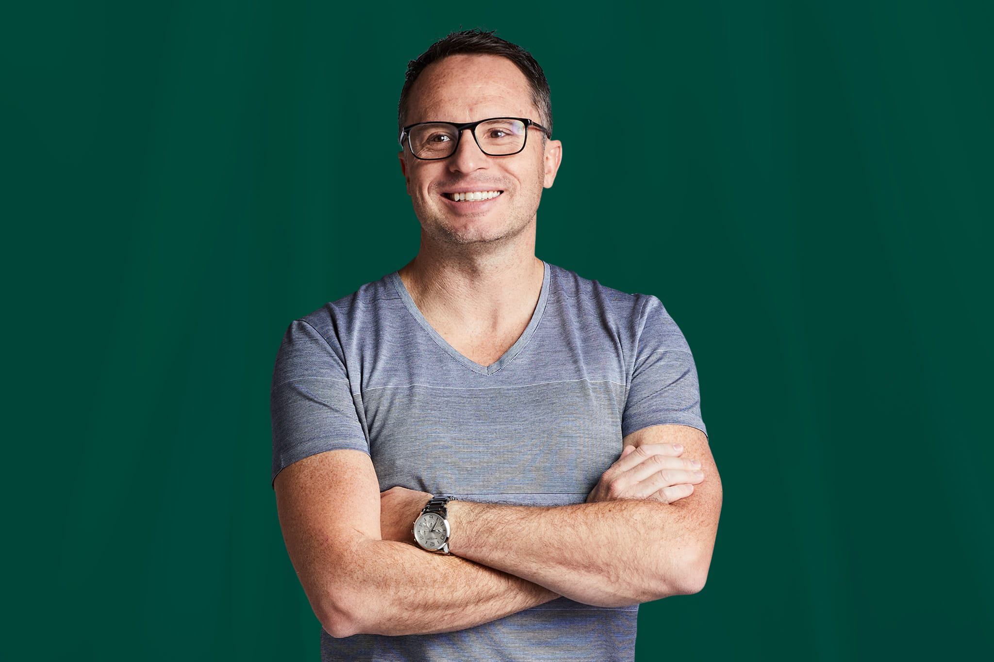 A man with glasses and a grey shirt standing with his arms crossed