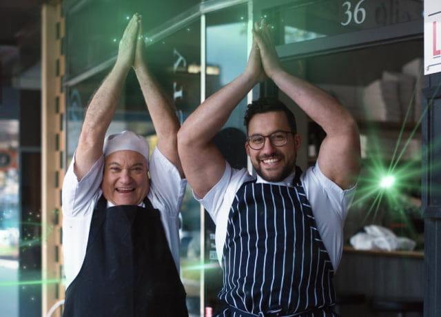 Two chefs in apron with hands up smiling