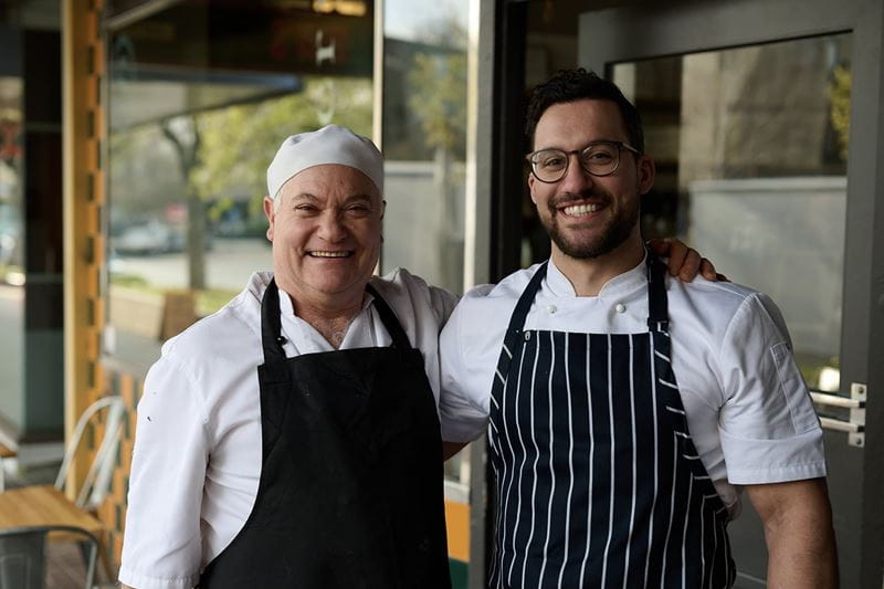 Two chefs in aprons standing in front of a restaurant