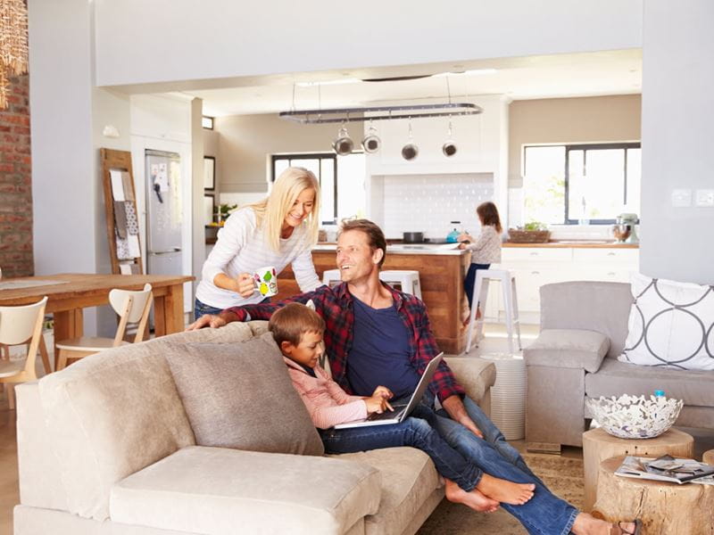 A family of 3 together at home sitting around the lounge with a laptop