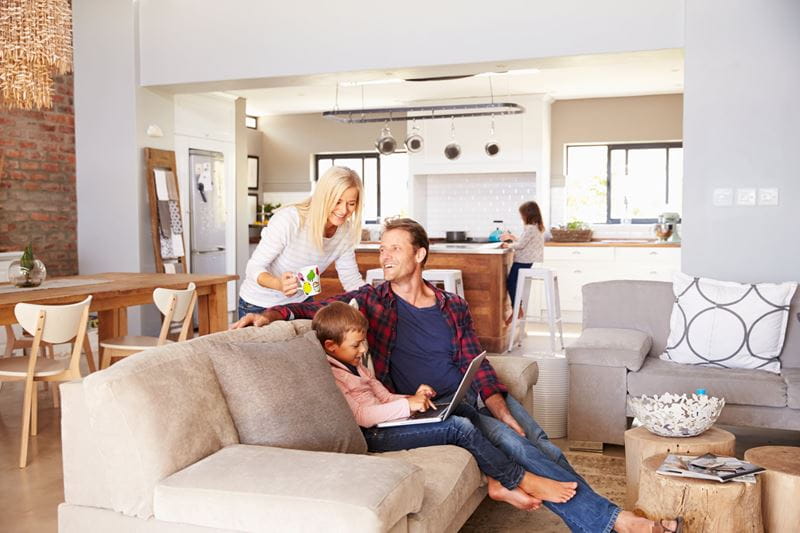 A family of three looking at a laptop screen while relaxing in their living room