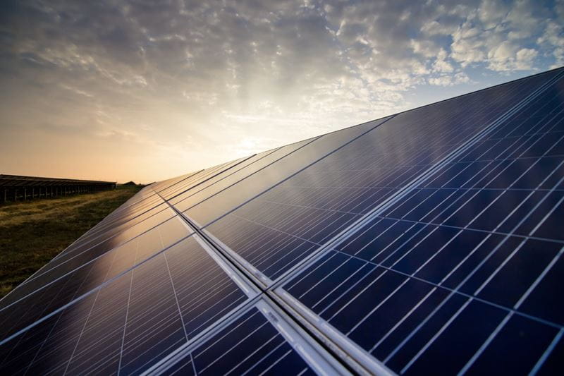 A close up of a solar panel with the sun setting in the background