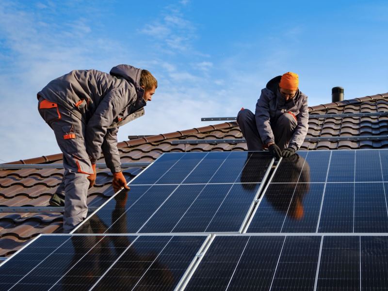 Two men are installing solar panels on a roof of a house