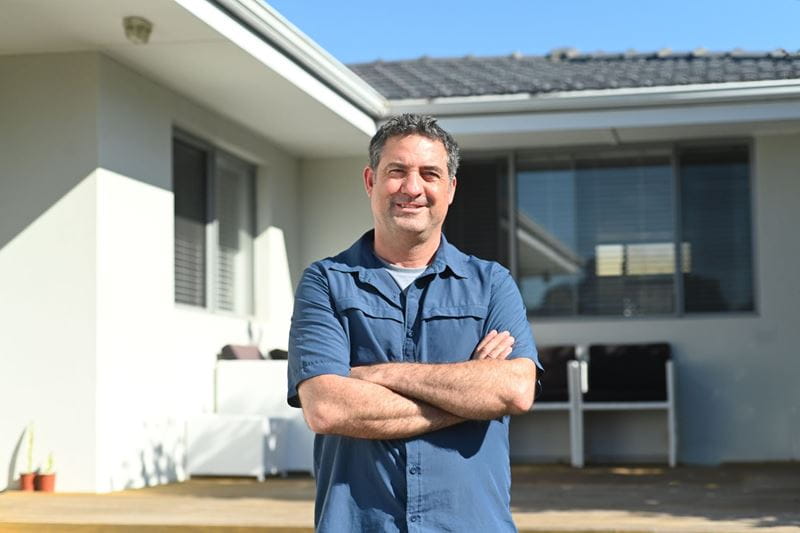 A man standing in front of a house with his arms crossed