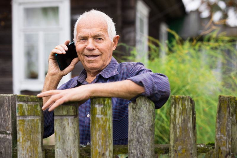 Man with purple shirt leaning over the fence talking on a mobile