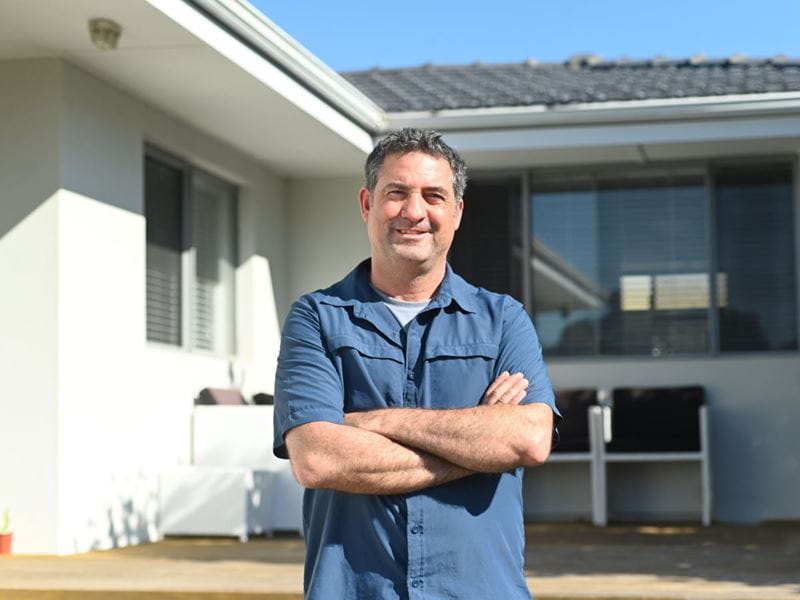A man smiling with his arms crossed outside a house 