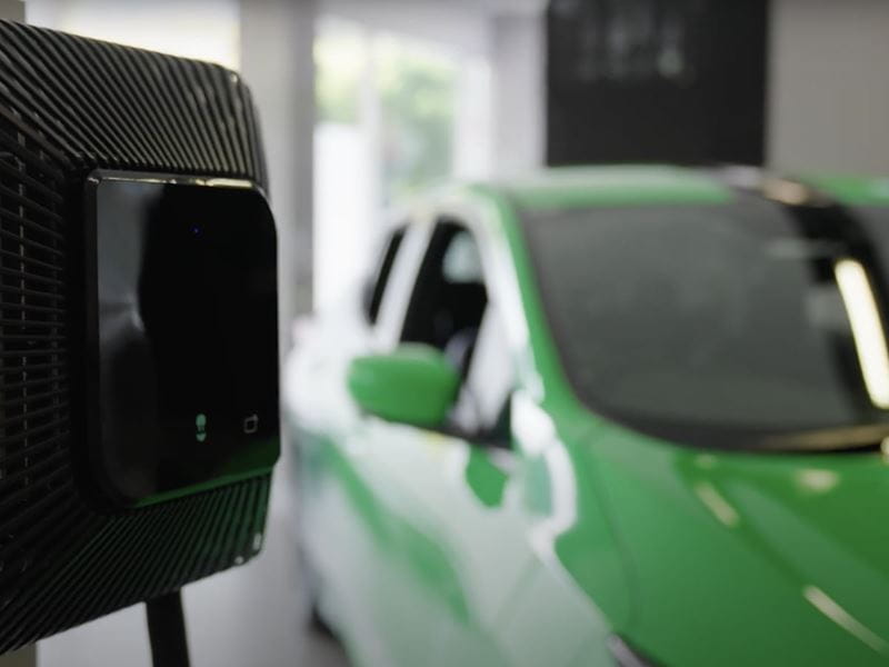 Electric vehicle home charger next to a green electric car