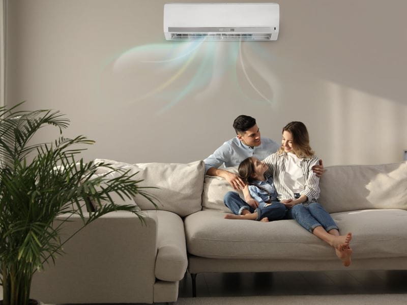 A family of three sitting on the lounge under the air conditioning unit