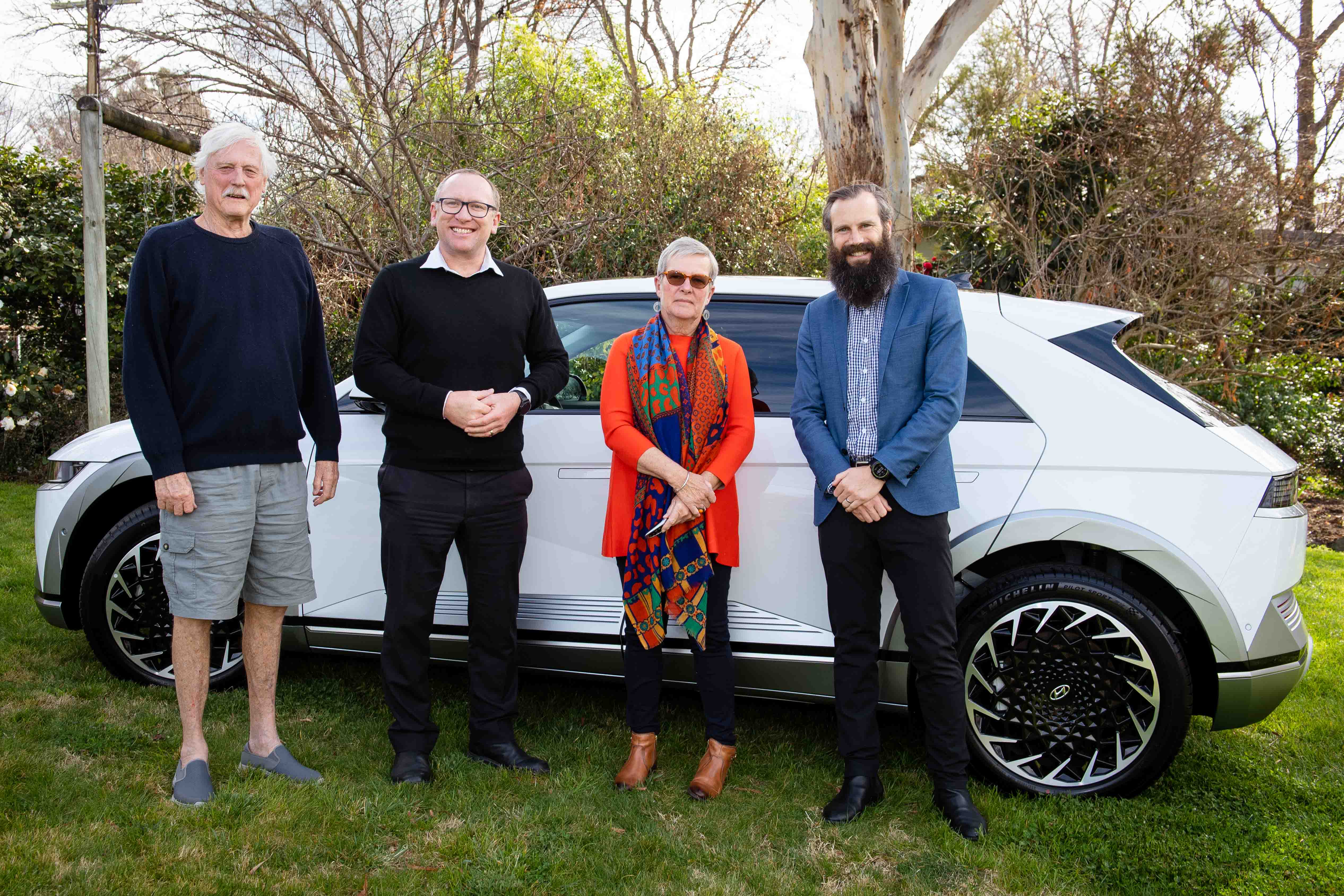 4 people standing in front of a electric vehicle.