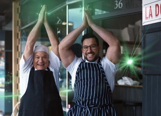 Two chefs in aprons clapping hands above their head