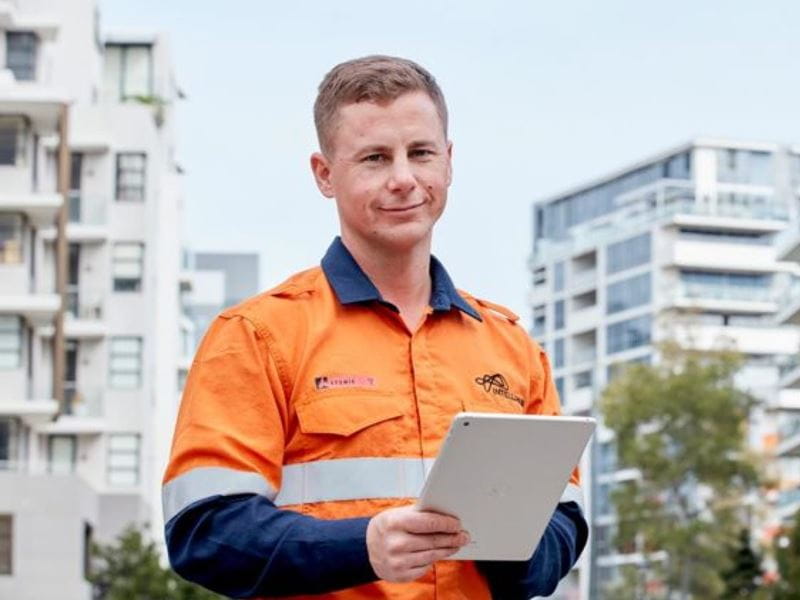 A man wearing an orange shirt, gripping a tablet