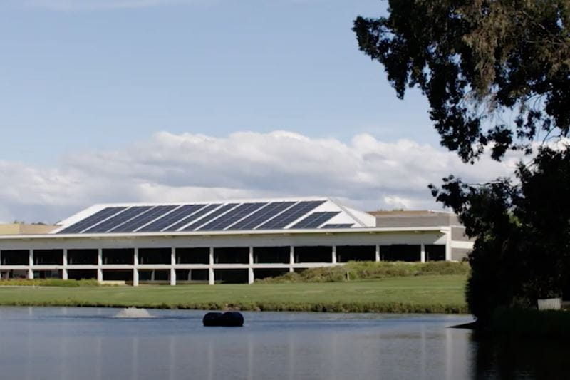 A large commercial building by the lake with solar panels. 