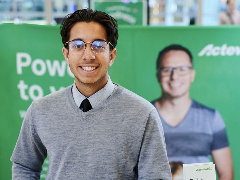 A man with black hair in front of ActewAGL banner.